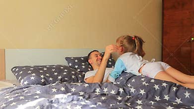Happy young father lifting cute little kid daughter up fly as airplane having fun together enjoying morning in bed