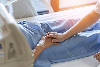Caregiver holding elderly senior patient ageing old adult person hand in hospital bed or nursing hospice, geriatrician