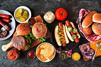 Summer BBQ food table with hot dog and hamburger buffet, flat lay over a dark background