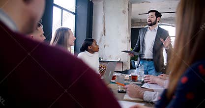 Handsome young professional Caucasian coach businessman leading multiethnic team at modern office meeting slow motion.