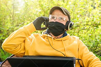 Old man in mask glasses adjusts headphones to listen music