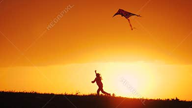 Silhouette of little girl launch kite, running on meadow at golden sunset