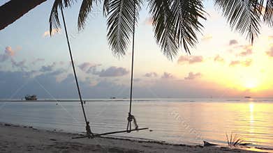 Great tropical beach. Sunset, a swing sways on a palm tree. Calmness and comfort. 4k video.