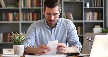 Focused young businessman in glasses doing accounting at office.