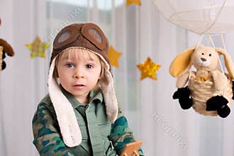 Sweet toddler boy, playing with airplane and teddy bear, air balloons with toys behind him