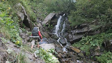Tourist with Backpack Came to Mountain Waterfall and Spreading Arms to Sides