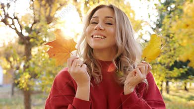 Woman in red dress hides face with yellow leaves in park