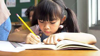 School girl sitting in school writing in book with pencil, studying, education, learning. Asian children in the class