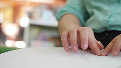 Close-up of disability blind person woman hands moving fingers reading Braille book studying in creative library. Braille is a