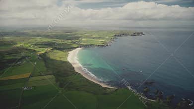 Ireland farmland, ocean bay aerial view: yellow fields, green meadows in Antrim. Cloudy summer sky