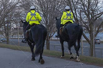Two mounted police officers riding horse on a sidewalk along city street.