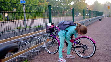The girl is trying to hang a lock on a bicycle