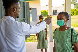 School teacher wearing a lab coat, taking temperature reading of school pupil