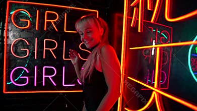 Joyful go-go dancer woman is flirting with camera, portrait against signboard of nightclub with neon lights