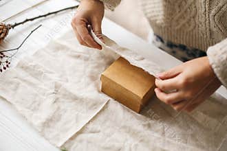 Plastic free christmas present, zero waste  holidays. Female hands in cozy sweater wrapping christmas gift in linen fabric on