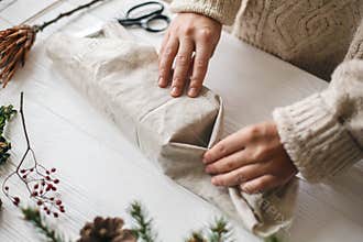 Plastic free christmas present, zero waste  holidays. Female hands in cozy sweater wrapping christmas gift in linen fabric on