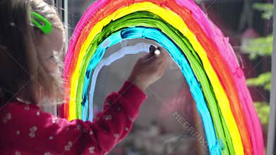 Girl draws a rainbow with paints on the window