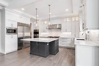 A white luxury kitchen with lights hanging above the island.