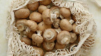 Young fresh Champignons in a ecological zero-waste net bag placed on beige background