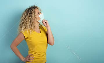 Woman with mask has doubt about covid19 virus. Cyan background.