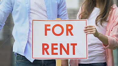 Husband and wife setting for rent sign and hugging outdoors, private property
