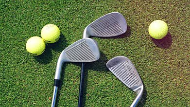 Golf balls and clubs on a grass at a golf course.
