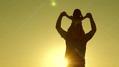 Dad carries beloved baby on his shoulders walking around field at sunset. little daughter riding with dad on his