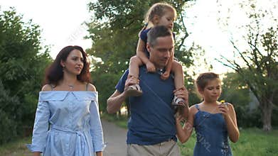 Husband and wife for a walk with their children. A little girl sits on her fathers shoulders. Happy family vacation