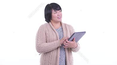 Happy overweight Asian woman thinking while using digital tablet ready for winter