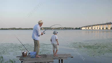 Happy childhood, loving dad spends time with his dear son fishing on pier by river during summer vacations in