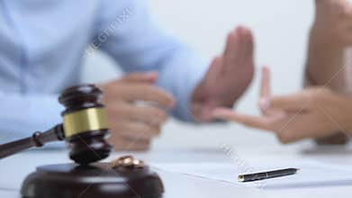 Couple arguing in court, gavel with engagement rings on table, divorce concept