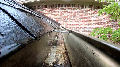 Water flowing thru gutter off shingled roof