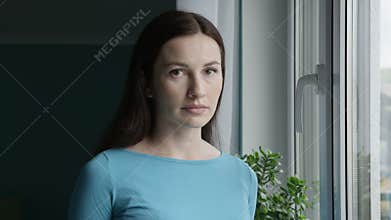 Portrait of Troubled Woman with Sad Neutral Face Expression Standing at the Window Looking at Camera Shot on Red