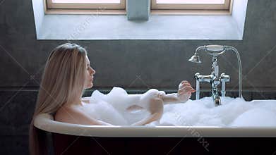 Beautiful blond woman lies in a bath with foam and relaxes.