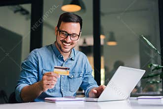 Happy cheerful smiling young adult man doing online shopping or e-shopping satisfied entrepreneur making online payment paying for