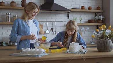 Mom and daughter bake muffins in the kitchen together. A woman puts the dough in a selikon baking dish with a wooden