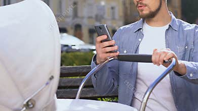 Smiling man with stroller choosing baby staffs on smartphone, online shopping