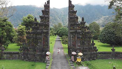 Aerial view of happy tourist woman with drone running through bali traditional gate in bedugul Traditional Balinese