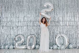 Smiling beautiful young pregnant girl posing holding figures 2020 at bright silver background