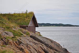 Rocky coast of Norwegian sea with the traditional Scandinavian turf roof construction in the background
