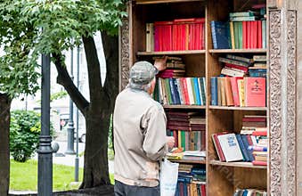 Russia, Vladivostok, 07/06/2019. A man stands by the wooden street cabinet with free books. Books in the cabinet are free, anyone