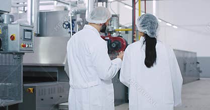 Charismatic engineer man and his assistance in a big manufacturing industry walking through the factory and analyzing