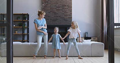 Happy young woman dancing with overjoyed daughters in living room.