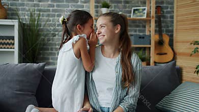Adorable girl whispering secret in mother's ear smiling hugging expressing love