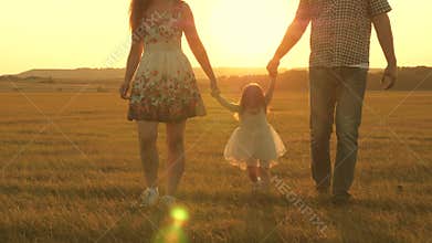 Little daughter jumping holding hands of dad and mom in park on background of sun. Family concept. child plays with dad