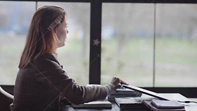 Portrait of a tired girl, a business woman is nervous because of hard work online sitting at table by window in an