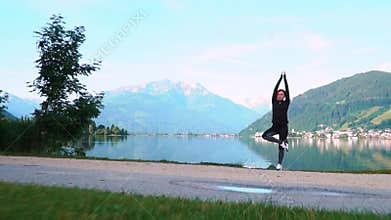 An attractive young woman doing a yoga pose for balance and stretching near the lake Zell am See high in the Alpine mountains in A