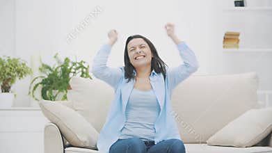 Young woman rejoices sitting on sofa, she won a price. 4K.