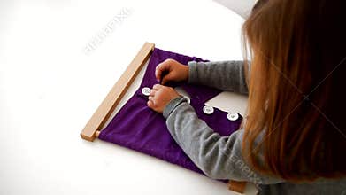 Little girl in a montessori school buttoning a frame with fabrics and buttons