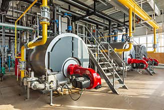 The interior of an industrial boiler room with three large boilers, many pipes, valves and sensors